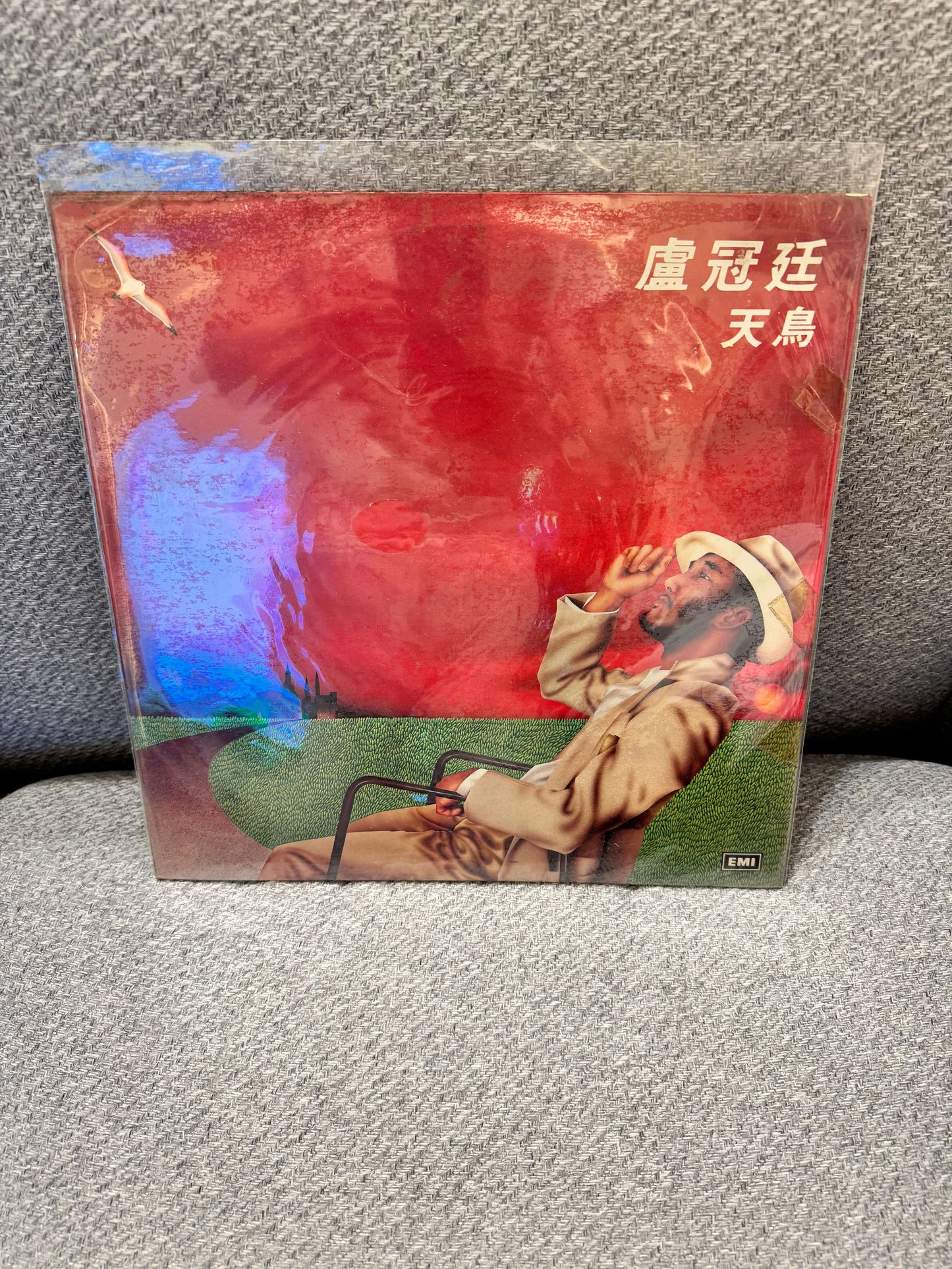 盧冠廷 – 天鳥 Album Cover featuring a man in a hat, enjoying the view with a vibrant red background.